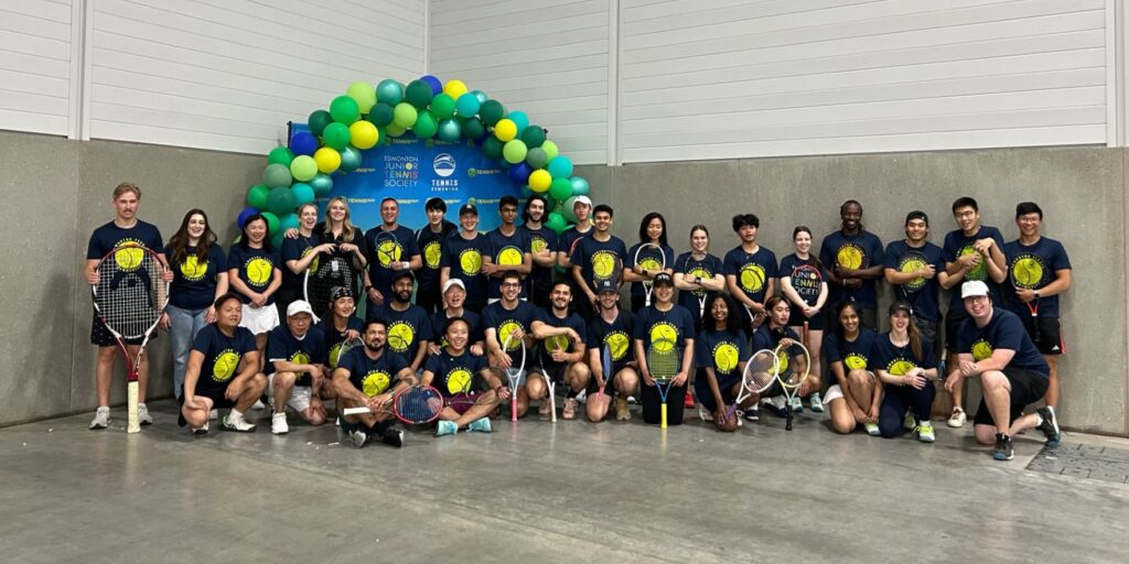 A large group of tennis enthusiasts pose together with their matching shirts.