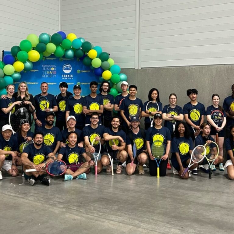 A large group of tennis enthusiasts pose together with their matching shirts.